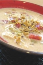 A bowl of creamy chicken enchilada soup topped with crushed tortilla chips.