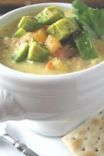 A bowl of chicken corn chowder topped with creamy avocado served with crackers on the side