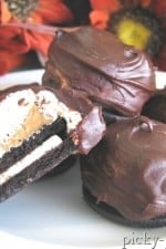 A few Chocolate, Peanut Butter, and Marshmallow Oreos on a plate with one cut in half so you can see the inside.