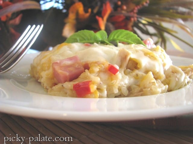 A serving of cheesy chicken cordon bleu rice casserole topped with fresh herbs on a white plate