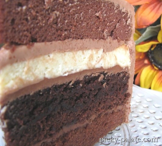 A close up of Double Chocolate Cheesecake Layer Cake showing the layers of chocolate cake, frosting, cheesecake, and brownie.
