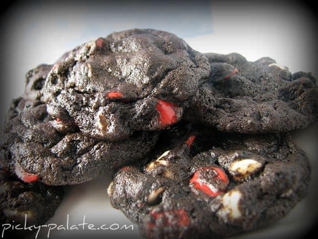 A pile of rich Chocolate Cherry Chip Cookies with bursts of red cherry chips and white chocolate chips mixed throughout.