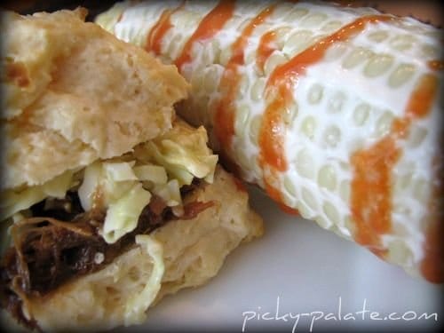 An Extreme Close-up of Spicy Corn on the Cob Beside a Biscuit Pulled Pork Sandwich