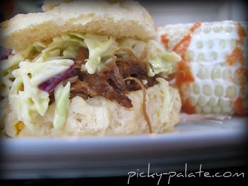A Pulled Pork Sandwich with Coleslaw and Spicy Corn on a White Plate
