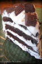 Slice of layered chocolate cake with cream cheese frosting and peanut butter cups.