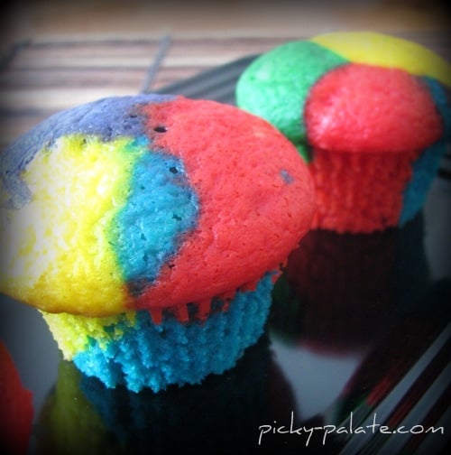Two red, blue, yellow, and green cupcakes on a plate.