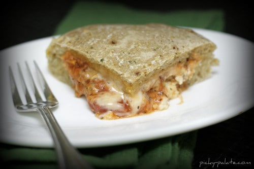 A serving of sausage lasagna stuffed pizza on a plate next to a fork.