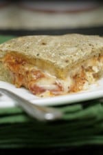 A serving of sausage lasagna stuffed pizza on a plate next to a fork.