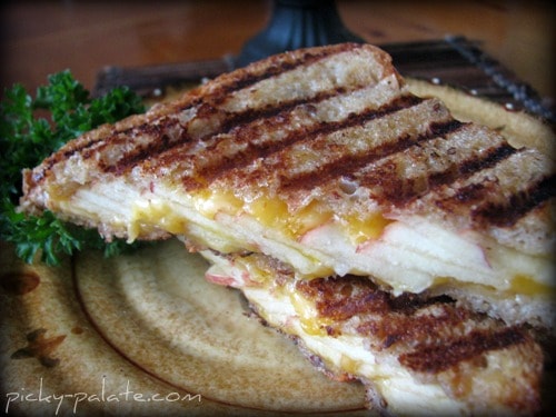 Apple cheddar panini sliced in half on a plate.