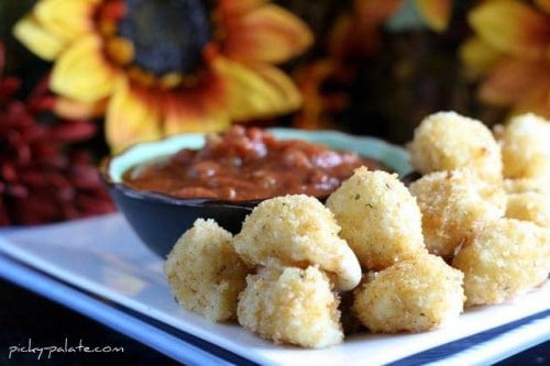 A pile of fried mozzarella balls on a plate next to a bowl of marinara sauce.