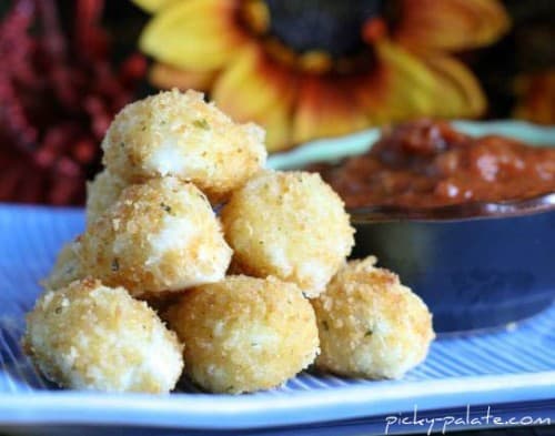 A stack of fried mozzarella balls on a plate next to a bowl of marinara sauce.