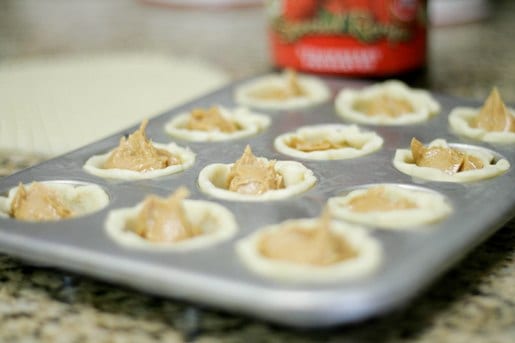 A mini muffin tin filled with pie crusts and peanut butter.