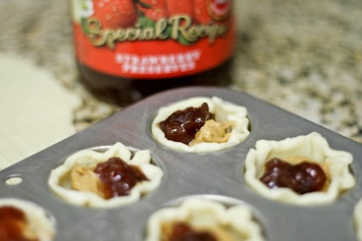 A muffin tin with mini pie crusts filled with peanut butter and jelly.