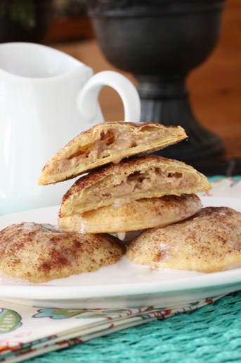 A pile of cinnamon roll hand pies on a plate, drizzled with vanilla icing.