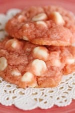 Two pink white chocolate chip cookies on a chip cookies on a doily.