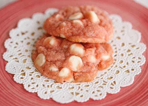 Two pink white chocolate chip cookies on a chip cookies on a doily.