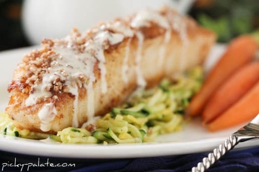 A Chilean sea bass fillet crusted with pecans and Dijon on a plate, served over zucchini slaw and baby carrots.