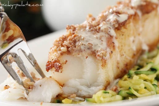 A fork picks up a piece of crusted Chilean sea bass from a plate.