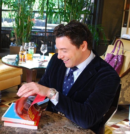 Rocco DiSpirito Smiling While Flipping Through His Cookbook