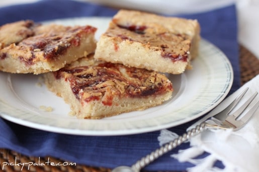 Three peanut butter and jelly shortbread cookie bars on a white plate, next to a fork.