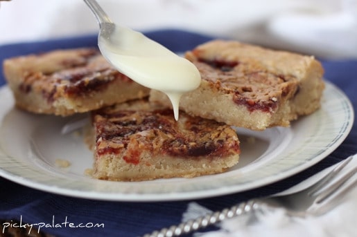 Three peanut butter and jelly shortbread cookie bars are drizzled with glaze on a plate.