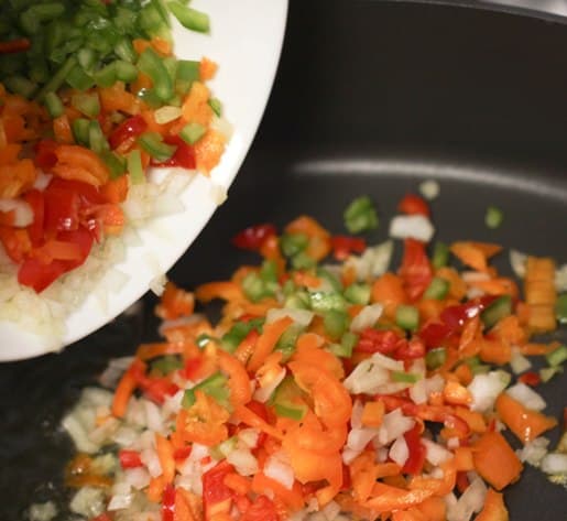 Veggies are added into a skillet.