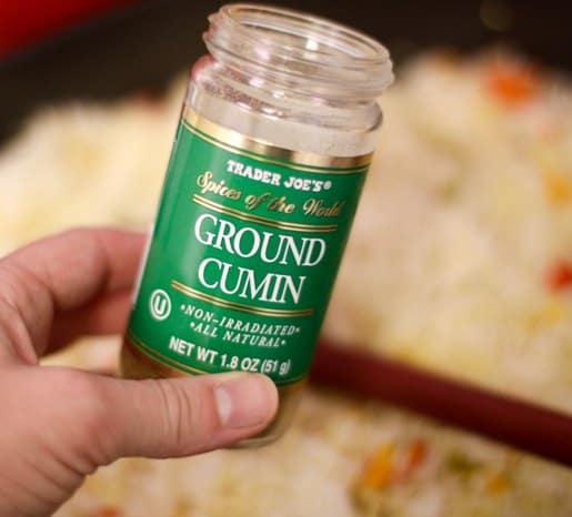 A hand holding a spice jar of ground cumin.