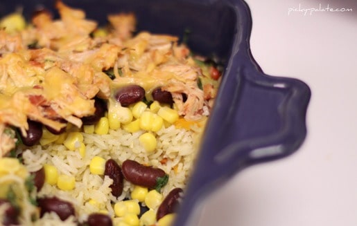 Shredded chicken is added to a casserole dish over top of rice and beans.