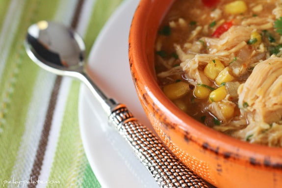 A Close-Up of a Bowl of BBQ Chicken Pizza Soup Next to a Metal Spoon