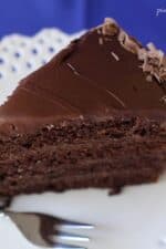 A slice of 4-layer chocolate cake with frosting on a plate