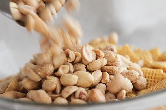Roasted peanuts are added into a bowl of Chex mix.