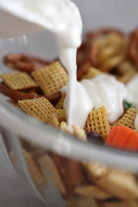 Melted vanilla candy is poured over top Chex mix in a mixing bowl.