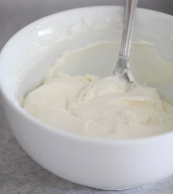 Cream cheese mixture in a white mixing bowl with a spoon.