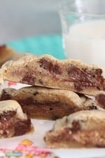 Candy bar chocolate chip cookies cut in half so you can see the candy sandwiched in between the baked dough. There is a glass of milk in the back.