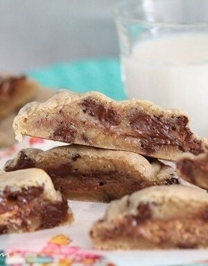 Candy bar chocolate chip cookies cut in half so you can see the candy sandwiched in between the baked dough. There is a glass of milk in the back.