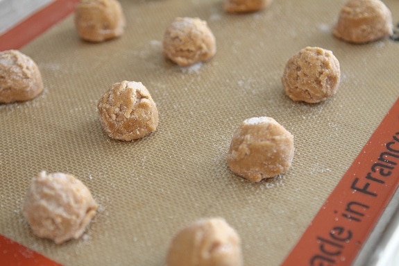 Peanut butter cookie dough balls lined up on a silicone baking mat.
