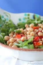 Chickpea, sweet pepper and arugula salad in a white bowl.