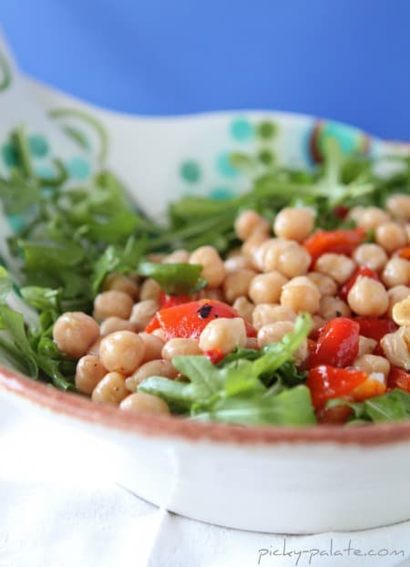 Chickpea, sweet pepper and arugula salad in a white bowl.