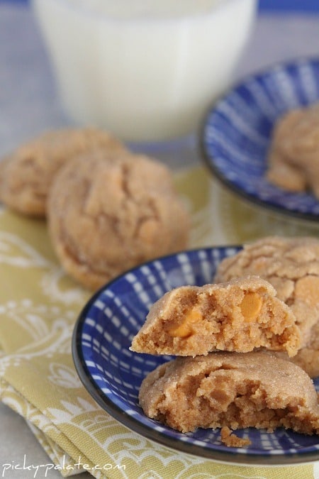 Butterscotch peanut butter cookies stacked on a blue plate, with a glass of milk and more cookies in the background.