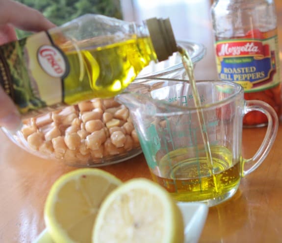 Olive oil is poured into a measuring cup surrounded by lemons.