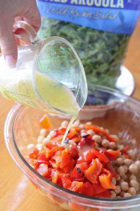 Lemon dressing is poured over a bowl of chickpeas and red peppers.