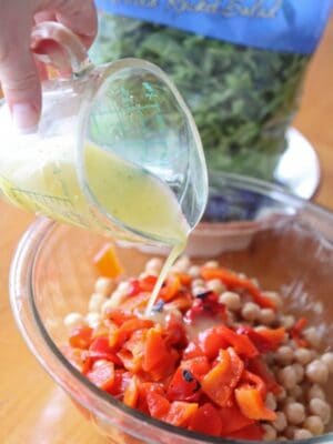 Lemon dressing is poured over a bowl of chickpeas and red peppers.