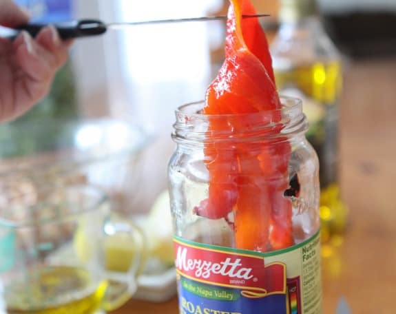 Roasted red peppers are lifted out of a jar.