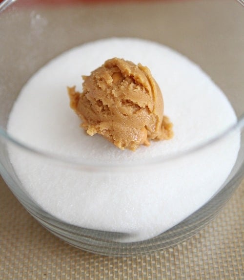 Peanut butter cookie dough ready to roll in a bowl full of sugar.