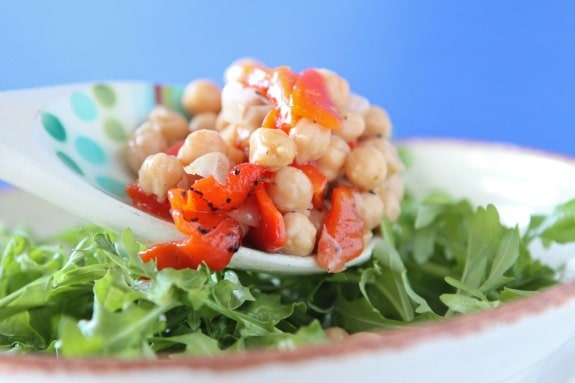 A spoonful of chickpeas and sweet peppers is added to arugula salad.