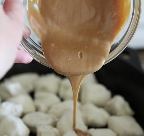 Melted peanut butter is poured over pieces of sugared biscuit dough in a skillet.