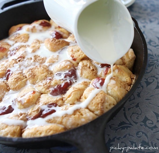 A cream glaze is poured overtop peanut butter and jelly monkey bread in a skillet.