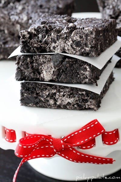 Three cookies and cream bars stacked on a white cake stand with a red ribbon.