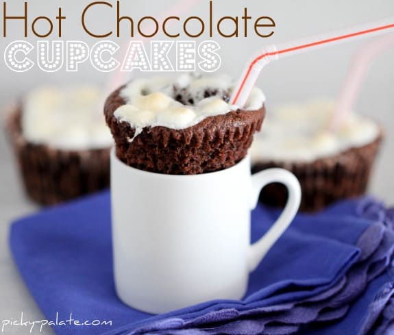 A hot chocolate cupcake perched on top of a white mug with a red and white striped straw.