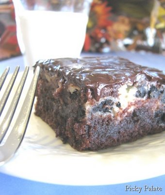 A Cookies and Cream Swirled Brownie topped with a Chocolate and Peanut Butter Ganache with a fork and glass of milk.